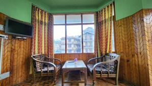 A room with a large window, two chairs, a small table, and a television mounted on the wall. - Hotel Jubilant Manali (Manali)