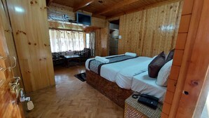 A wooden cabin with two beds, a small table, and a TV mounted on the wall. - Hotel Jubilant Manali (Manali)