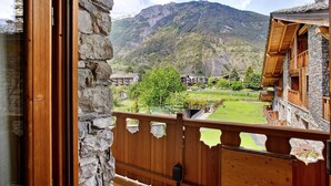 A wooden balcony with a stone wall, a view of a mountain, and a green lawn.