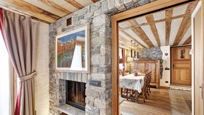 A stone fireplace with a framed painting above it, wooden beams on the ceiling, and a dining area with a table and chairs.