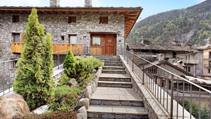 A stone building with a wooden door, a staircase leading to a balcony, and a mountainous backdrop.