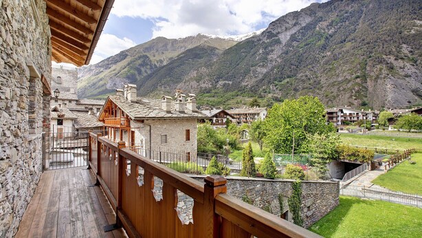 A balcony with stone walls, wooden railings, and a view of a mountainous landscape.