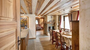A rustic interior with exposed wooden beams, a dining area with a table and chairs, and a cozy living space with a fireplace.