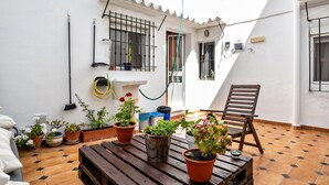 A patio with potted plants, a wooden table, a chair, and a white wall with a window and a door. - Holiday Home "Calle Ancha" with Private Terrace & Wi-Fi (Barbate)