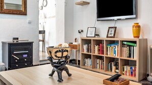 A modern living room with a wooden table, a television mounted on the wall, a bookshelf filled with books, and a decorative bowl on the table. - Holiday Home "Calle Ancha" with Private Terrace & Wi-Fi (Barbate)