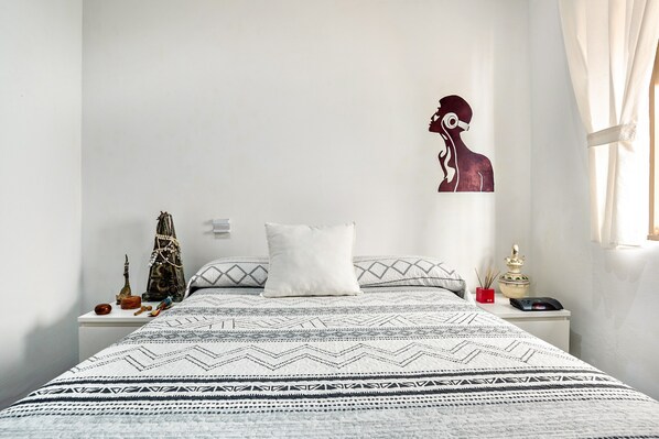 Een net opgemaakt bed met beddengoed met een patroon, een wit kussen en een decoratief object op het nachtkastje.