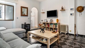 A living room with a sofa, a wooden coffee table, a bookshelf, a television, and a radiator. - Holiday Home "Calle Ancha" with Private Terrace & Wi-Fi (Barbate)