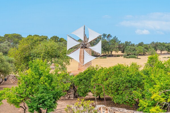 A windmill with white sails in a rural setting with trees and a clear sky. - Villa 'Garraseca' with Mountain Views, Wi-Fi and Air Conditioning (Llucmajor)