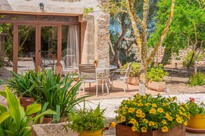 Une terrasse avec une table et des chaises, entourée de plantes en pot et d’un mur de pierre.