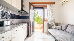 Eine kleine Küche mit Toaster, Spüle und Schränken, die auf einen Balkon mit Stuhl und einem Bett mit Kissen führt.