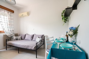 A bedroom with a bed, a table set for dining, and a wall-mounted air conditioner.