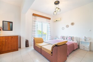 A bedroom with a bed, a sofa, a bedside table, a nightstand, a mirror, and a window with curtains.