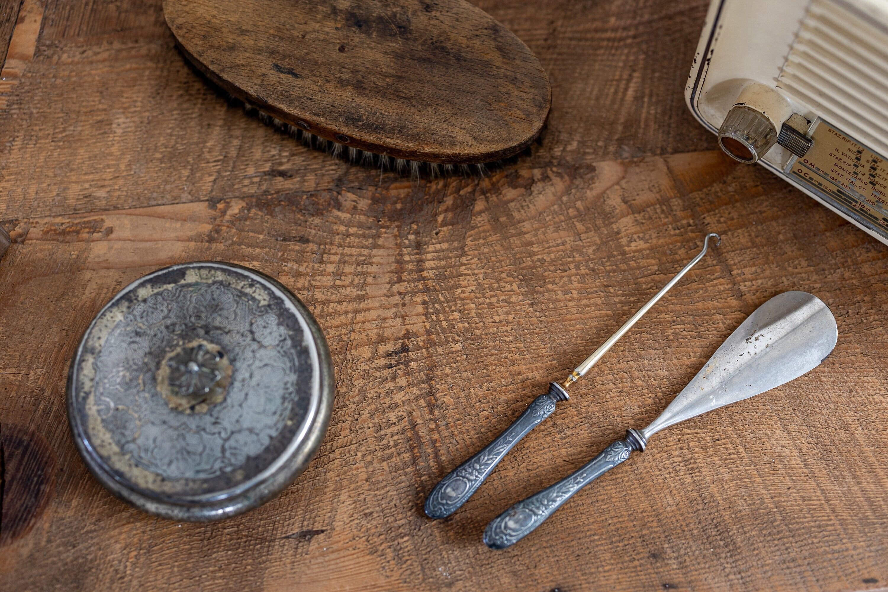 A wooden surface with a metal container, a brush, and a metal tool.