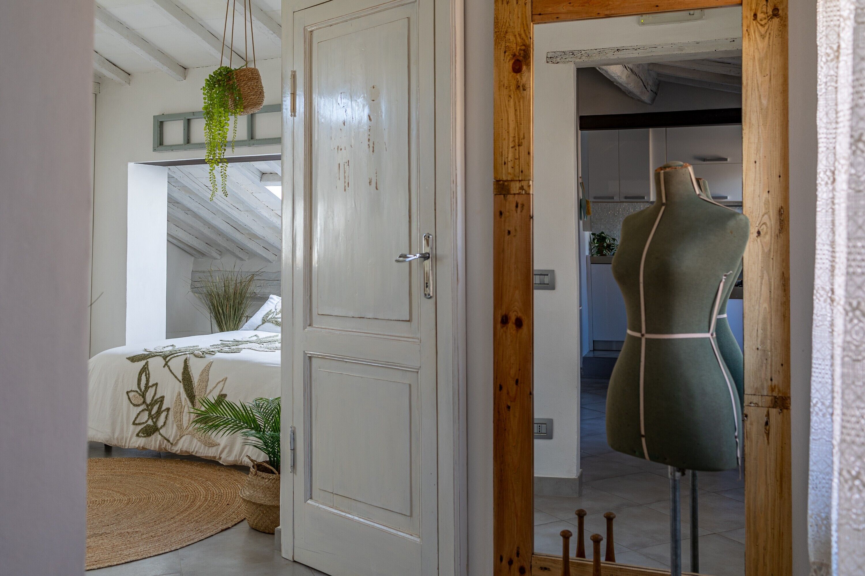 Ein Zimmer mit einem Bett, einer hängenden Pflanze, einer Mannequin und einem Holztürrahmen.