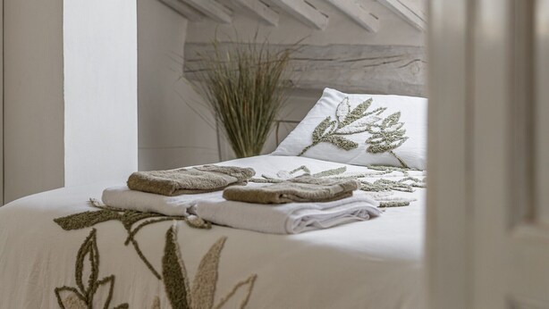 Un dormitorio con techo inclinado, una cama con colcha estampada con motivos de hojas y una planta en maceta.