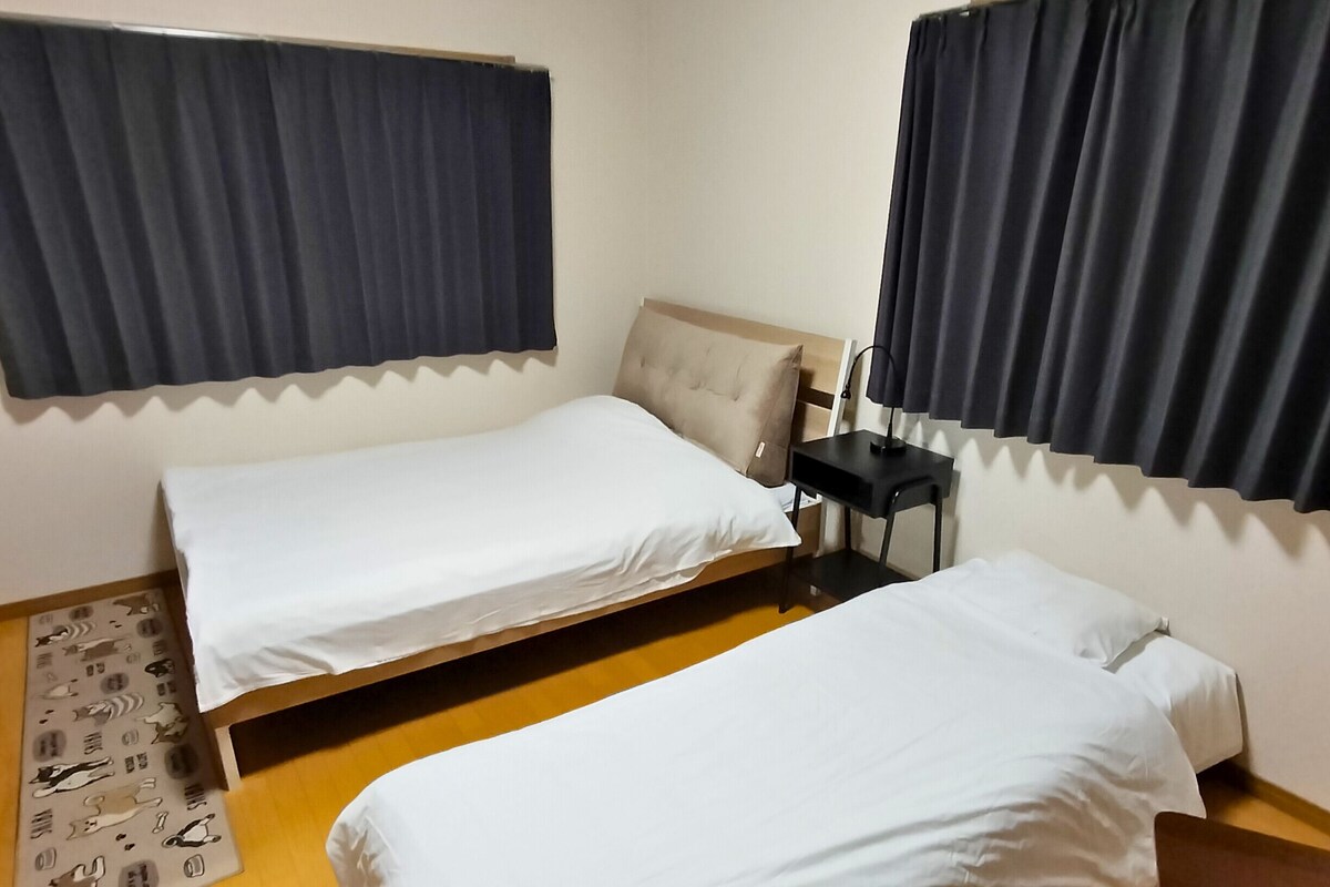 A room with two single beds, a small table, and a chair.