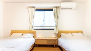 A hotel room with two single beds, a wooden nightstand, a window with curtains, and an air conditioning unit. - Minamiaoyama 1st (Tokyo)