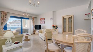 A living room with a sofa, a dining table with chairs, a TV, and a view of the outside. - Apartment 'La Terraza del Mar' with Sea View, Wi-Fi and Air Conditioning (Manilva)