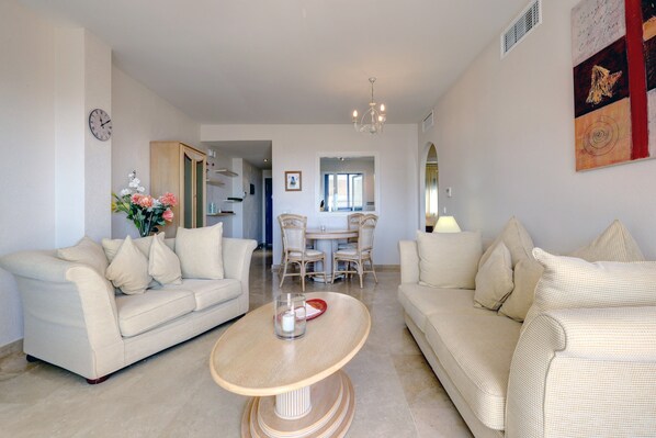 A living room with two sofas, a coffee table, a dining table with chairs, and a chandelier.
