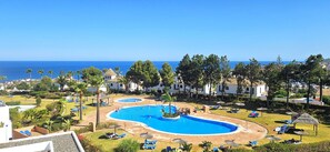 A resort with a large central pool, smaller surrounding pools, and a view of the sea.