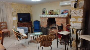 A living room with a TV, fireplace, wicker chairs, and a dining table.