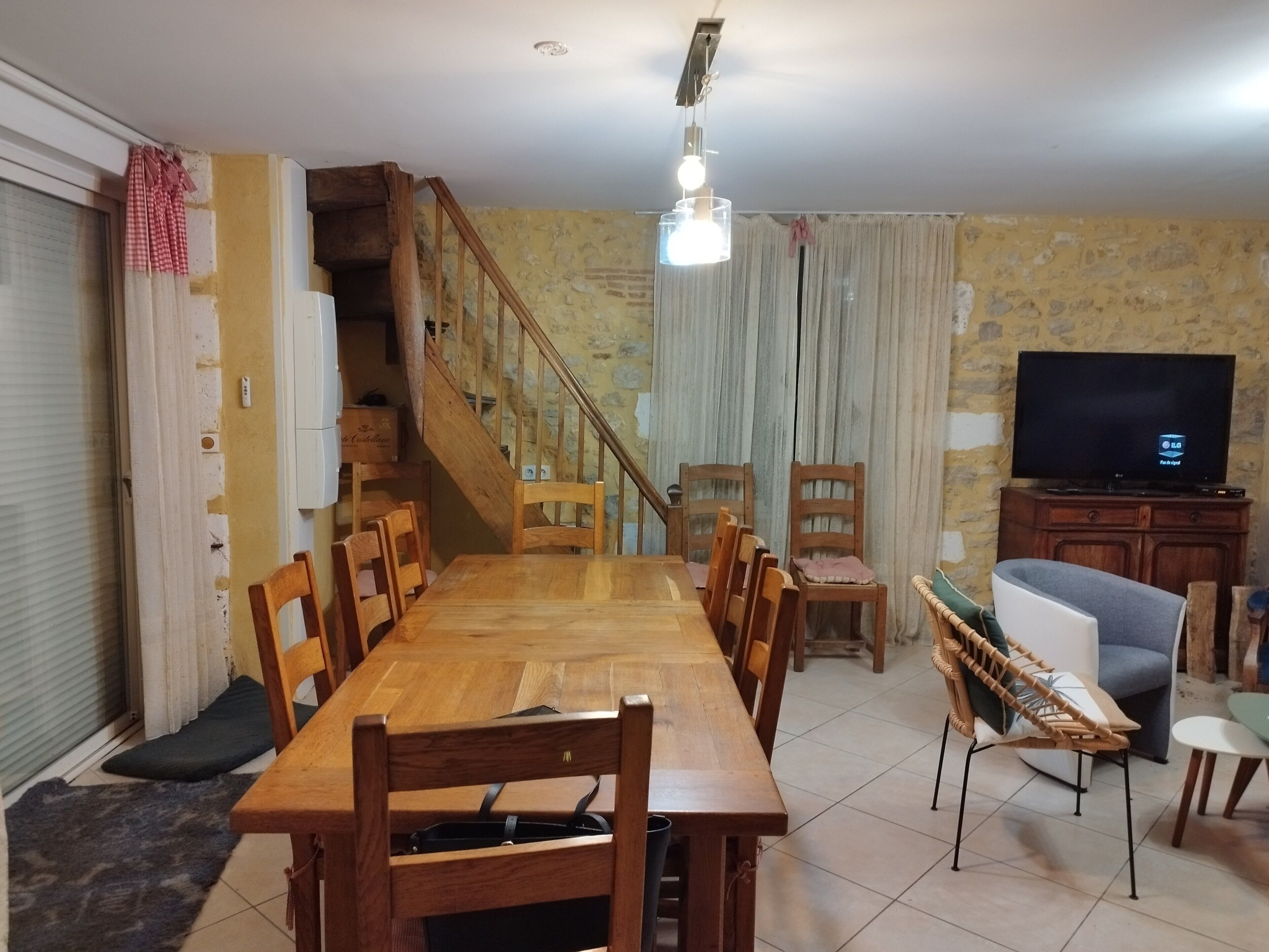 Ein Essbereich mit Holztisch und Stühlen, einer Treppe, einem Fernseher und einem Sofa.