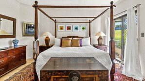 Un lit à baldaquin avec une couette blanche, deux tables de chevet avec des lampes, une commode en bois et un tapis à motifs.
