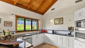 Une cuisine moderne avec des armoires blanches, une grande fenêtre et un plafond en bois.