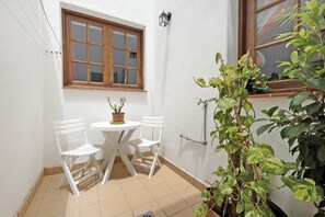 A small patio with a table and two chairs, a window, and potted plants.