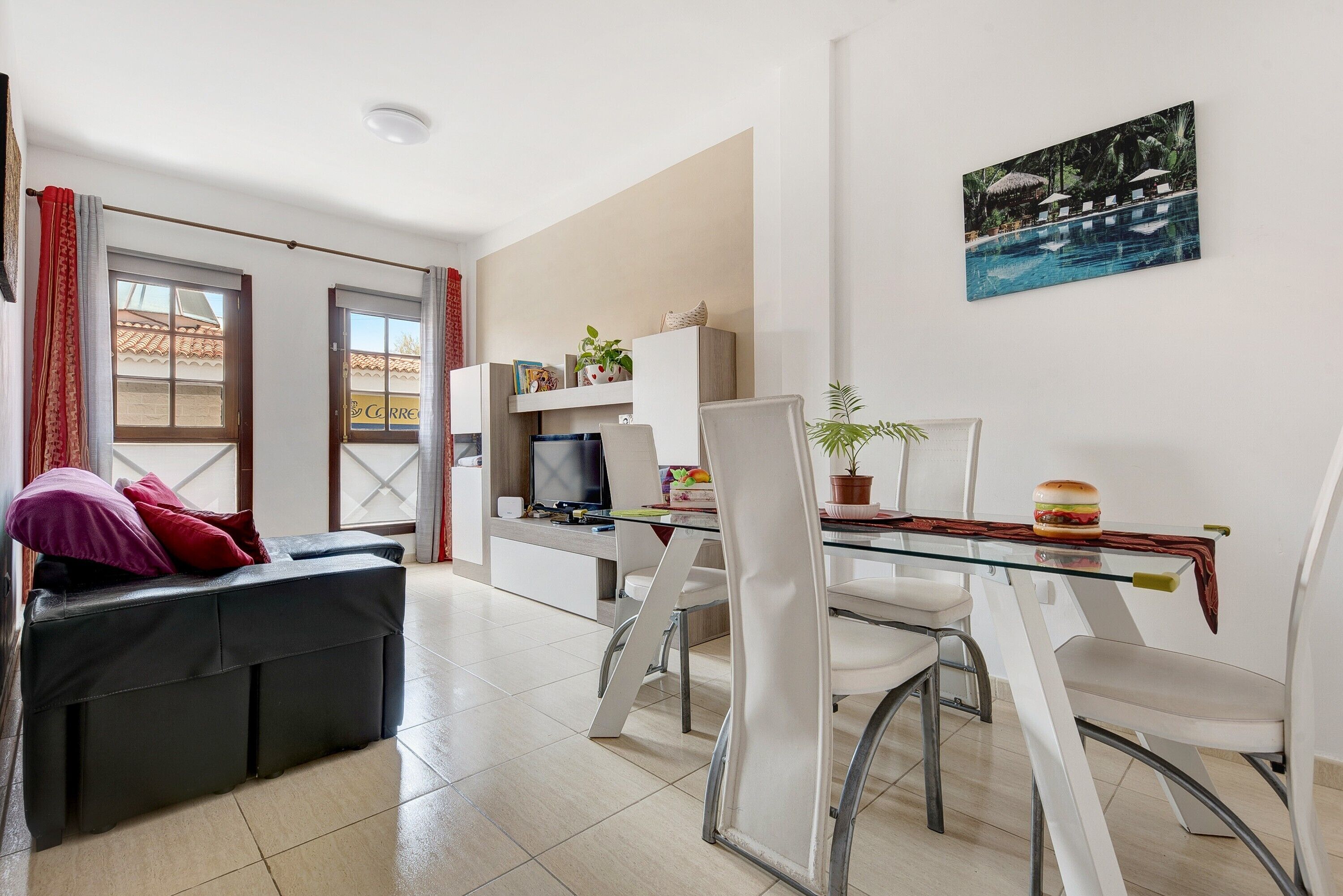 Een moderne woonkamer met een glazen eettafel, witte stoelen, een zwarte bank en een televisie.