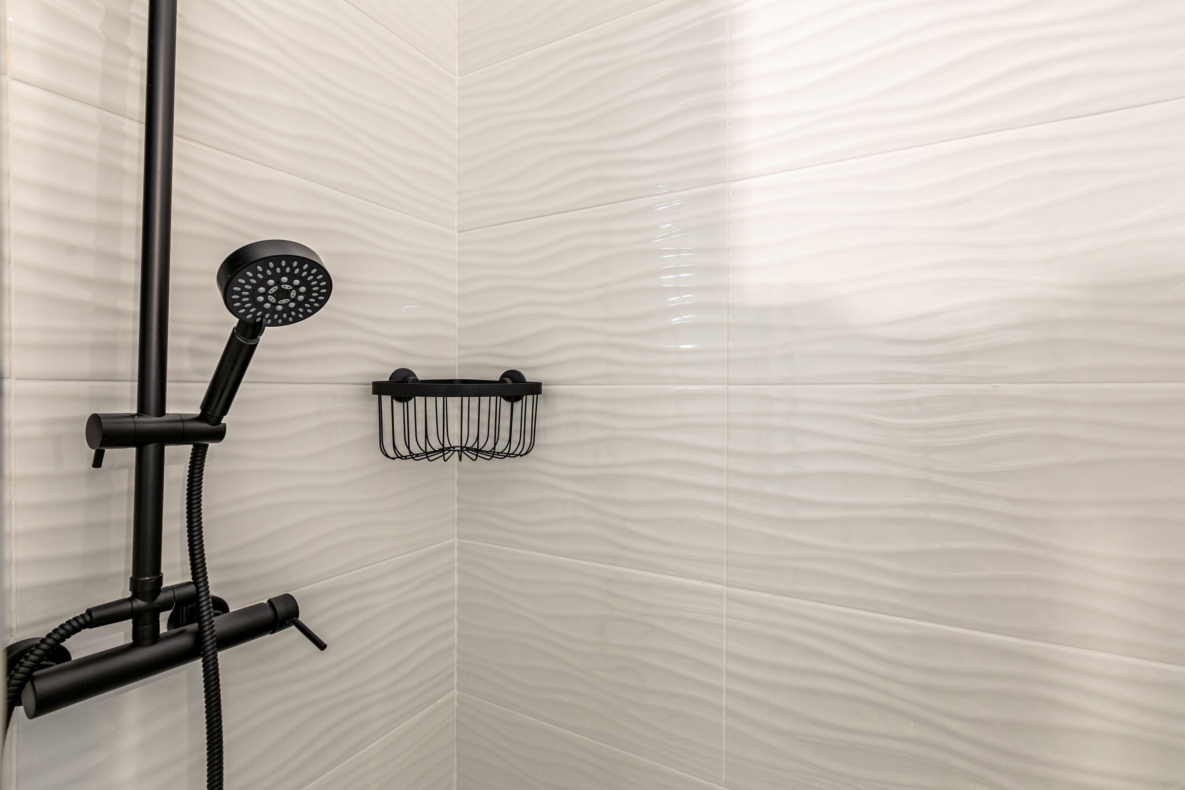 A shower with a handheld showerhead, a wall-mounted towel rack, and a textured wall.