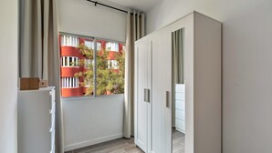 Een moderne kamer met een garderobe, een raam met gordijnen en uitzicht op gebouwen.