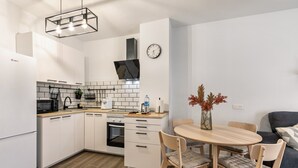 Een moderne keuken met witte kastjes, een zwarte magnetron en een houten eettafel met stoelen.
