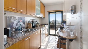A kitchen with wooden cabinets, a granite countertop, stainless steel appliances, and a dining area with a table and chairs. - Apartment "Sunset House Algarve" with Private Terrace & Wi-Fi (Faro)