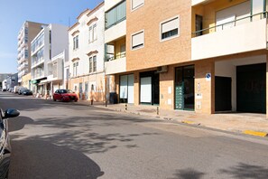 Une vue de rue avec des immeubles à plusieurs étages, une voiture rouge garée sur le bord et un ciel dégagé.