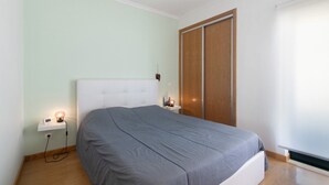 A bedroom with a bed, bedside table, lamp, and a sliding door. - Apartment "Sunset House Algarve" with Private Terrace & Wi-Fi (Faro)