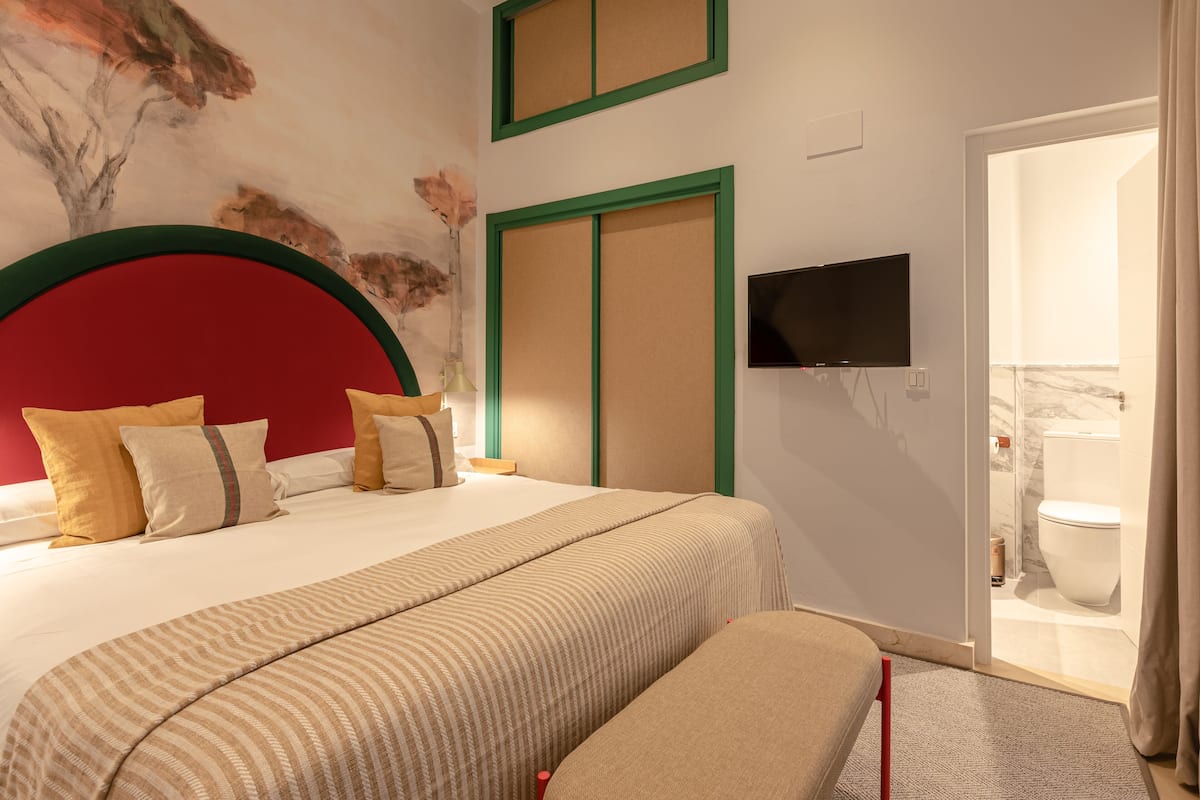 Habitación de hotel con una cama grande, un televisor montado en la pared y un baño visible a través de una puerta abierta.