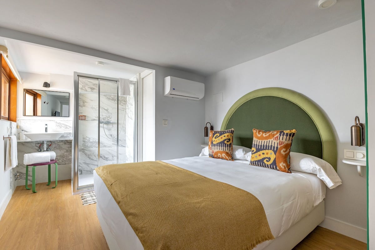 Un dormitorio moderno con una cama grande, un cabecero verde y un baño con ducha de vidrio y lavamanos de mármol.