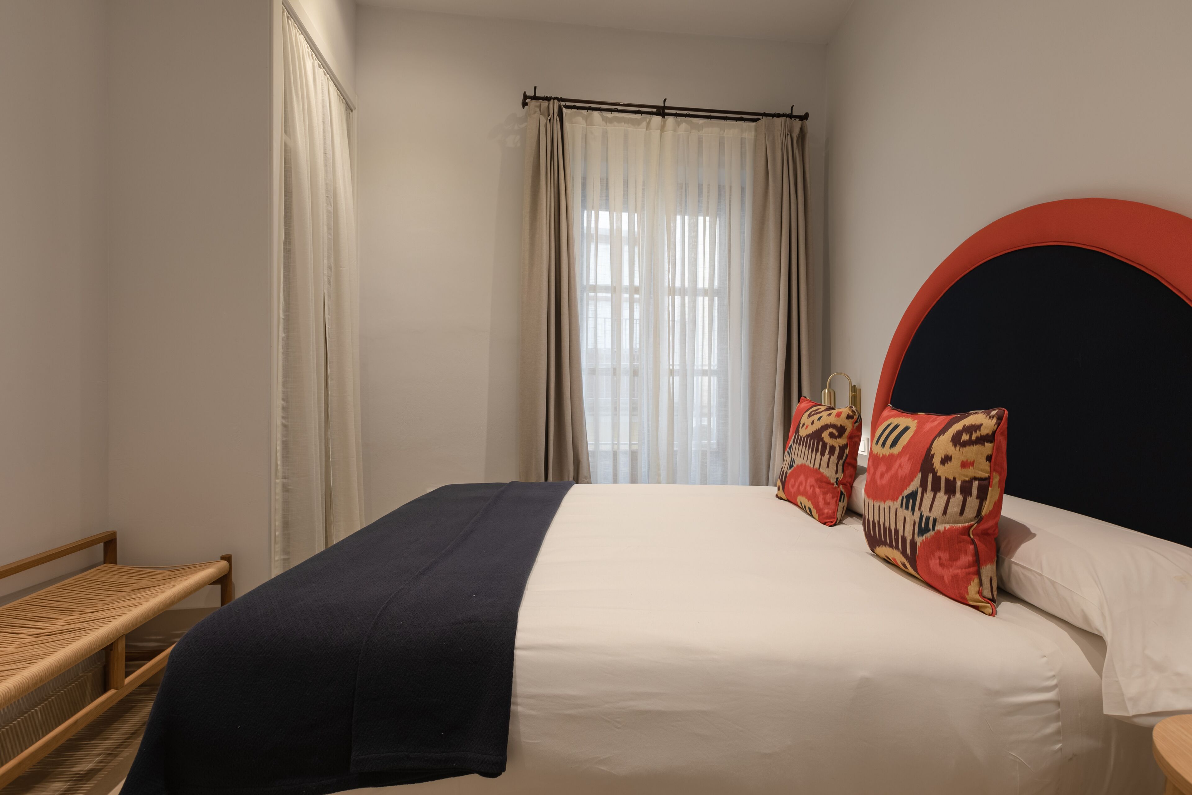 A bedroom with a bed, a bedside table, a window with curtains, and a headboard.