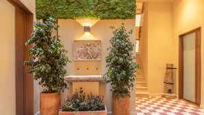 Un pasillo con suelo a cuadros, plantas en macetas, una escultura en la pared y una escalera.