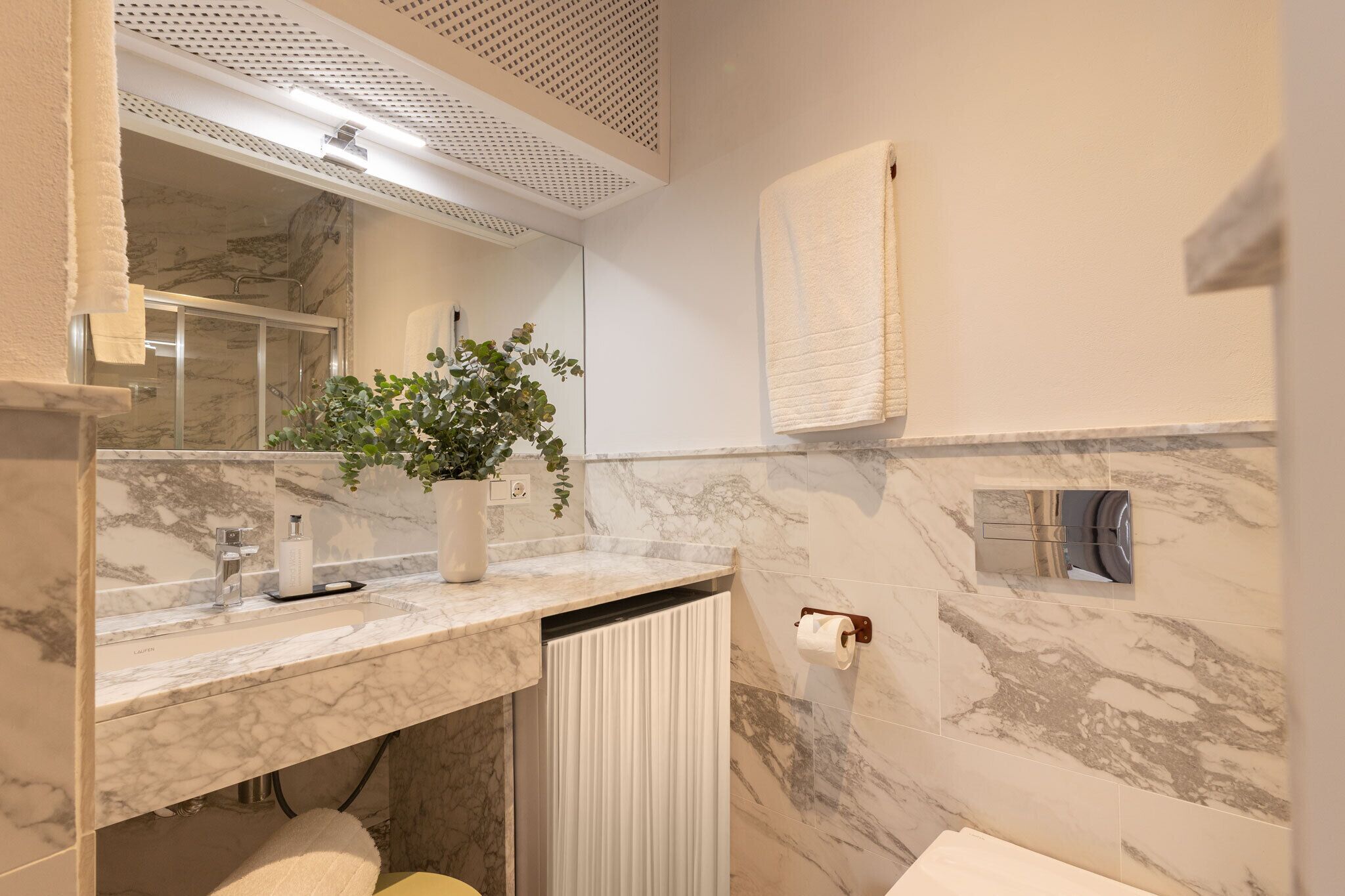 A modern bathroom with a marble sink, a potted plant, a towel rack, and a toilet paper holder.