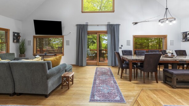 Un vaste espace de vie comprenant un canapé, une table à manger et des chaises. On y trouve une grande fenêtre avec des rideaux, un téléviseur et un lustre.