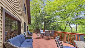 Une terrasse en bois, aménagée avec du mobilier d’extérieur, notamment un canapé et des fauteuils, qui offre une vue sur un paysage verdoyant et luxuriant.
