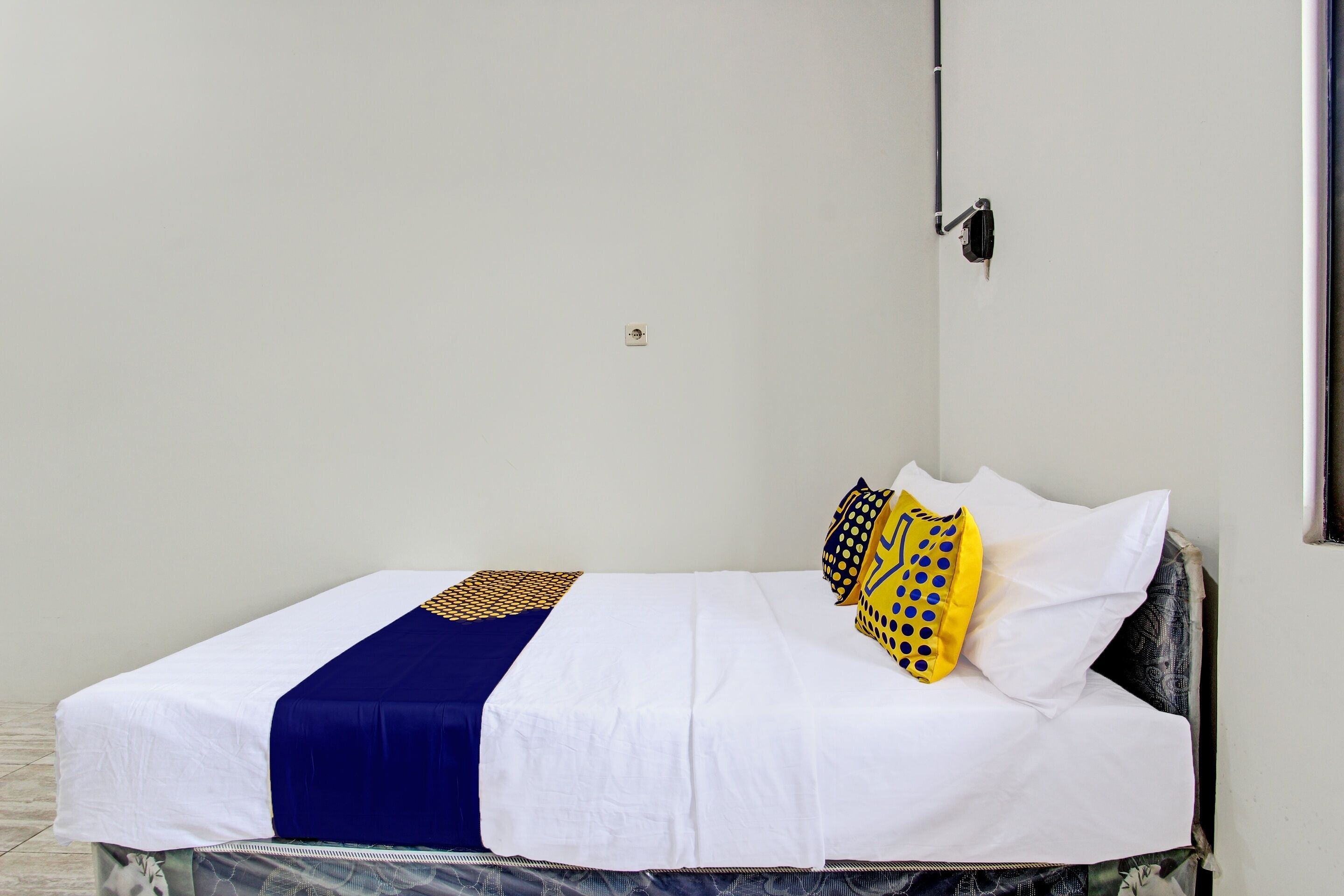 Una cama individual con colcha blanca y azul, un cojín estampado y cabecera negra.