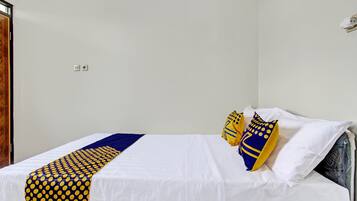 A single bed with white bedding, a blue and yellow patterned throw, and two decorative pillows.