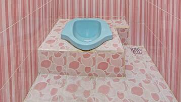 Un baño pequeño con baldosas rosas y blancas a rayas, un inodoro asiático azul y una lámpara de techo blanca.