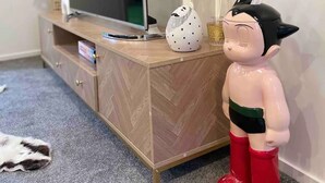 A wooden TV stand with a flat-screen TV, a white vase with dried plants, and a figurine.