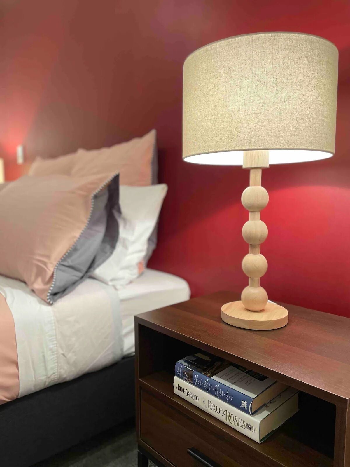 A bedside table with a lamp, a book, and a bed with pillows.