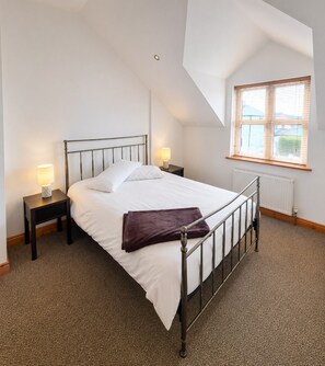 A bedroom with a bed, two bedside tables, a window, and a radiator. - Kilkee Townhouse (Kilkee)
