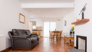 A living room with a leather sofa, a dining table with chairs, a fireplace, and a kitchen in the background. - Kilkee Townhouse (Kilkee)